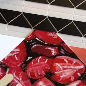 May include: A rectangular tile sheet featuring a geometric pattern of black triangles and white horizontal bars. Below this, a portion of a card displays a painted illustration of red strawberries on a black background with white highlights.
