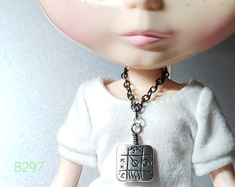 May include: A doll with green eyes and pink cheeks wearing a white shirt and a silver necklace with a square pendant featuring a design of symbols.