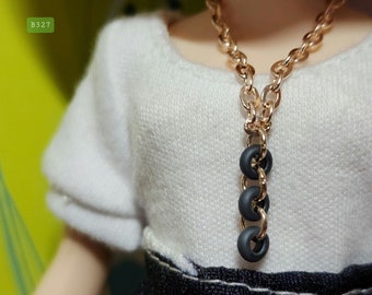 May include: A gold chain necklace with a pendant made of four black rings. The necklace is worn by a person wearing a white shirt.