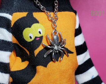 May include: A black and orange striped shirt with a black bat design and a silver spider pendant necklace.