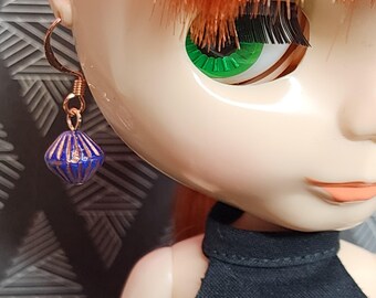 May include: A doll with orange hair and green eyes wearing a gold earring with a blue and gold bead. The doll is wearing a black sleeveless top.