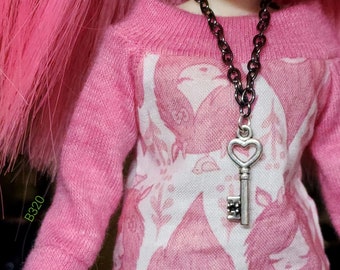 May include: A pink sweater with a white print of birds and flowers. A silver key charm hangs from a black chain necklace.