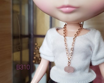 May include: A rose gold chain necklace with a light pink stone pendant. The necklace is worn by a doll with a white shirt.