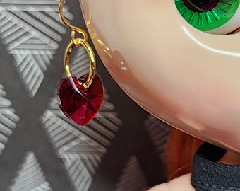 May include: Gold hoop earrings with a dangling red heart-shaped crystal.