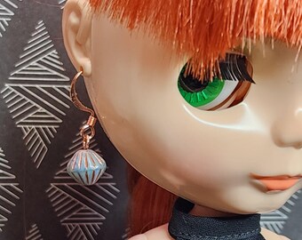 May include: A doll with red hair wearing a black dress and a pair of blue and gold earrings. The earrings are a single bead with a geometric pattern.