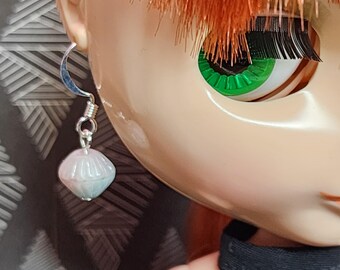 May include: A doll with red hair and green eyes wearing a silver earring with a white and pink bead.