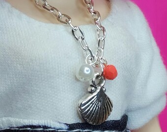 May include: A silver chain necklace with a silver seashell charm, a white pearl bead, and a red bead.