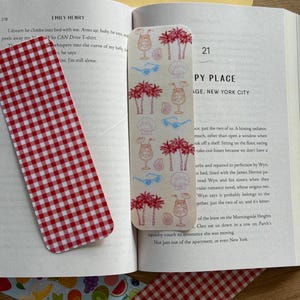 May include: A collection of bookmarks and decorative paper items. One bookmark features a red and white gingham pattern. Another bookmark has a cream background with illustrations of palm trees, cocktails, sunglasses, and seashells. Other paper items have fruit and striped patterns.