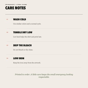 Op de afbeelding: Een witte informatiekaart met de titel CARE NOTES van CRYINGGHOST / LITERAL IDIOMS. Het bevat vier wasvoorschriften voor kleding: WASH COLD, TUMBLE DRY LOW, SKIP THE BLEACH en LOW IRON, elk met specifieke instructies en een laatste opmerking.