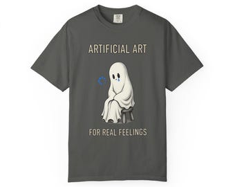 Op de afbeelding: Een antracietgrijs t-shirt met een afbeelding van een verdrietig wit spookje dat op een klein krukje zit. Boven het spookje staat de tekst ARTIFICIAL ART en eronder de tekst FOR REAL FEELINGS. Een klein blauw laadicoontje is zichtbaar.