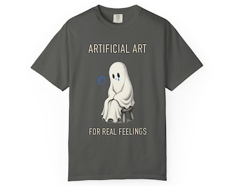 May include: A charcoal gray t-shirt featuring a graphic of a sad white ghost sitting on a small stool. Above the ghost is the text ARTIFICIAL ART and below is the text FOR REAL FEELINGS. A small blue loading circle icon is next to the ghost.