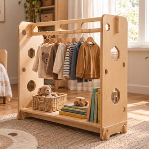 Puede incluir: Un perchero de madera de color claro para niños que cuenta con una barra horizontal con seis perchas de madera que sostienen varios suéteres y camisas, y un estante inferior con una cesta tejida que contiene un oso de peluche, libros y un coche de juguete.