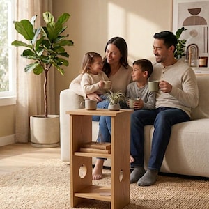 Peut inclure: Une table d'appoint en bois clair dotée d'un plateau rectangulaire, d'une étagère intermédiaire avec deux livres empilés et d'une étagère inférieure. Les panneaux latéraux présentent des découpes circulaires sur les deux niveaux inférieurs.