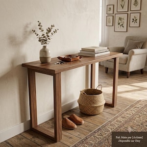 Op de afbeelding: Een rechthoekige houten sidetable met een donkerbruine afwerking en U-vormige poten. Op het oppervlak staan een keramische vaas met eucalyptus takken, een lederen schaaltje met sleutels en een stapel boeken. Een gevlochten mand staat op de vloer.