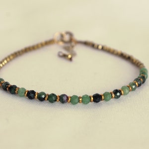 Może przedstawiać: Delikatna bransoletka z zielonymi i czarnymi koralikami z kamieni szlachetnych i złotymi akcentami.