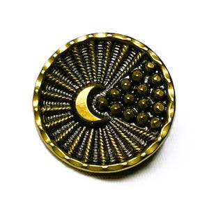 May include: A round, antique brass button with a crescent moon and beaded cluster design. The button has a textured, sunburst pattern radiating from the moon. The button is likely used for sewing or crafts.