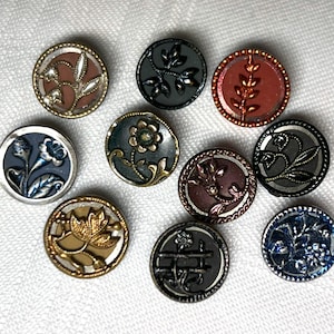 May include: A collection of decorative buttons with floral and leaf designs. The buttons are round, with metallic gold, silver, and bronze accents. The colors include shades of blue, brown, green, and red. The buttons are likely for sewing or crafts.