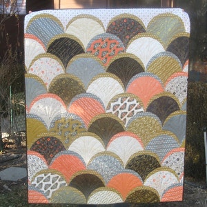 May include: A quilt with a fan-shaped pattern in shades of gray, brown, white, and orange. The quilt is made up of many individual fabric squares sewn together.