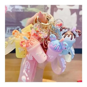 May include: A collection of colorful, cartoonish keychains featuring ice cream and drink designs. The keychains include a variety of colors, such as yellow, pink, and blue, with decorative elements like sprinkles and donuts. The keychains are attached to a gold-colored ring.