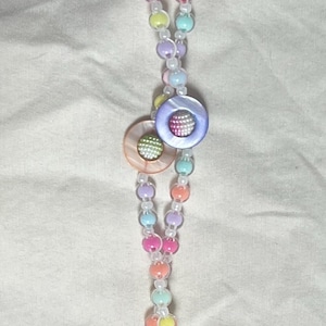 May include: A lanyard featuring a strand of multicoloured pastel beads in shades of pink, yellow, blue, and purple, interspersed with small white beads. The design includes four circular buttons with iridescent centres and a metal lobster clasp.