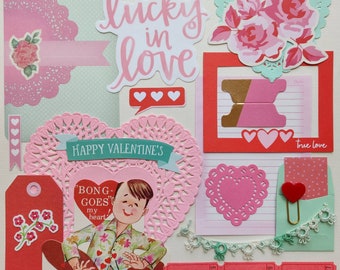 May include: A Valentine's Day scrapbook page with a pink and green color scheme. The page features a variety of paper crafts, including hearts, doilies, and a banner that reads "Happy Valentine's". There are also several stickers, including one that says "Lucky in Love".