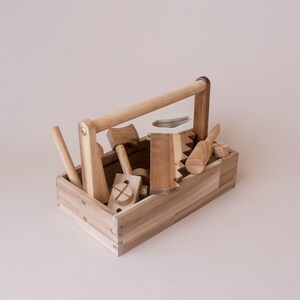 May include: A wooden toy toolbox filled with various wooden tools, including a hammer, saw, screwdriver, and more. The toolbox has a handle for easy carrying. The tools are made of natural wood and are designed for children.