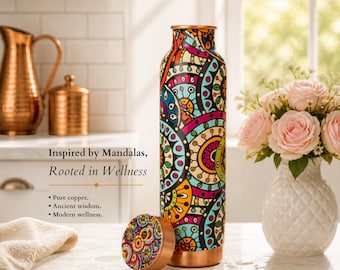 Op de afbeelding: Een koperen waterfles met een kleurrijk mandala-ontwerp, met de tekst "Mandala Harmony" en "900 ml". De fles wordt getoond met deksel, een vaas met roze rozen en andere koperen voorwerpen.