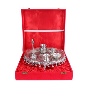 Puede incluir: Un juego religioso plateado, que incluye una bandeja, cuencos peque&ntilde;os y un soporte decorativo, presentado en una caja forrada de terciopelo rojo. El juego presenta patrones y dise&ntilde;os intrincados, ideal para ceremonias religiosas.