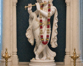Puede incluir: Una estatua de mármol blanco de una figura tocando una flauta dorada, adornada con una guirnalda floral, de pie en un arco tallado. Dos lámparas de aceite de latón flanquean la estatua, con un cuenco de flores amarillas y blancas.