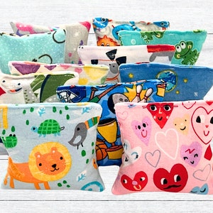 May include: A collection of 12 colorful fabric sensory bean bags with various patterns, including animals, sports, and hearts. The bean bags are all square and have a soft, plush texture.