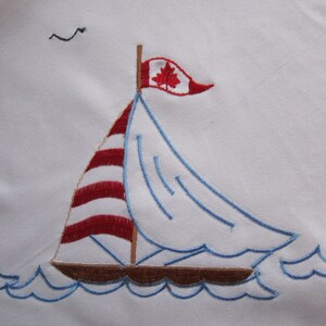 May include: Embroidered sailboat with a red and white striped sail and a Canadian flag. The sailboat is sailing on blue waves.