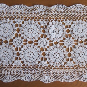 May include: White crocheted doily with a delicate floral pattern. The doily has a scalloped edge and is made with fine thread.
