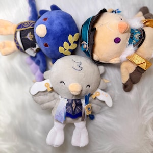 May include: A collection of plush toys in various character designs. The toys feature a variety of colors, including blue, beige, and white. The plushies have detailed facial features and clothing, with some featuring gold accents.