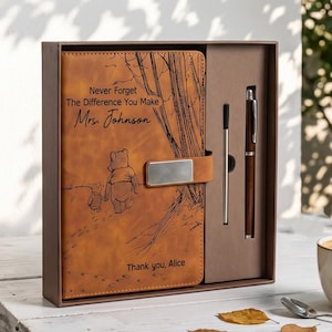 Peut inclure: Un carnet en similicuir beige dans une boîte brune, avec une fermeture métallique et une gravure représentant deux ours marchant. Le texte indique : Never Forget The Difference You Make Mrs. Johnson, et Thank you, Alice. Inclut un stylo.