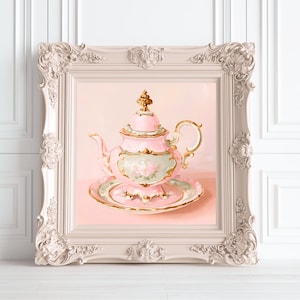 Puede incluir: Un cuadro enmarcado de una tetera de porcelana rosa con su plato a juego. La tetera presenta bordes dorados, un motivo floral en el cuerpo y una tapa con un remate dorado. El marco ornamentado de color claro tiene detalles tallados.