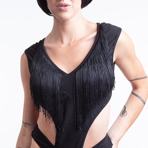 Peut inclure: Un body noir avec des détails en franges et des découpes. Le body a un décolleté en V et une silhouette ajustée.