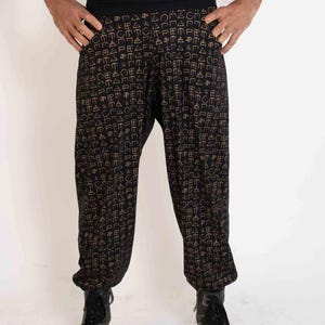 May include: Black harem pants with a repeating gold geometric pattern. The pants have a wide, black waistband and are worn with black boots. The fabric appears to be soft and flowing, suitable for casual wear.