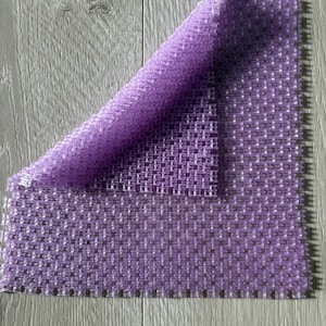 May include: A purple, square-shaped, textured bath mat with a grid pattern. The mat is folded in half and the texture is visible.