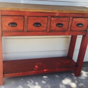May include: A red wooden console table with four drawers and a lower shelf. The drawers have black metal handles. The table has a distressed finish.