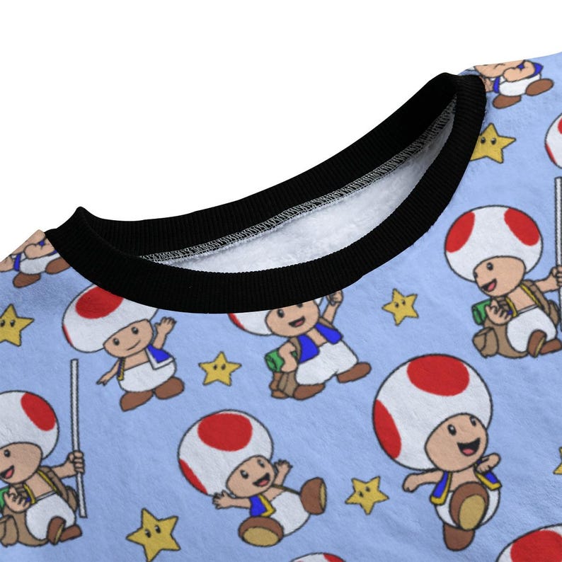 May include: Light blue sweatshirt featuring a repeating pattern of the character Toad from the Super Mario video game series. Toad has a white mushroom cap with red spots, a blue vest, and a tan backpack. Yellow stars are also scattered across the fabric.