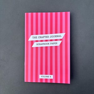 May include: A pink and fuchsia striped scrapbook paper journal titled "The Crafted Journal Scrapbook Paper Volume 4." The journal is rectangular and has a vertical striped pattern. The text is in white.