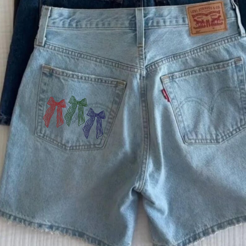以下が含まれることがあります： バックポケットに赤、緑、青の3つの刺繍リボンが付いた、ライトウォッシュデニムのショートパンツ。 ショーツはクラシックな5ポケットデザインで、Levi Strauss & Co.のラベルが付いています。