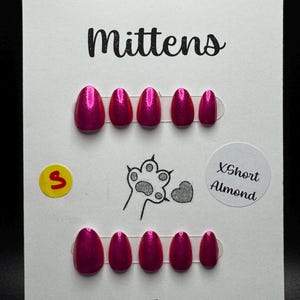 May include: A set of hot pink, almond-shaped press-on nails. The card reads "Murder Mittens" in black script. Additional text includes "ILNP - Petals", "XShort Almond", and a paw print design.
