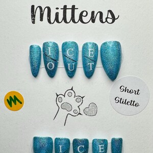 May include: A set of short stiletto-shaped false nails in a shimmering teal color. The nails are labeled "ICE OUT" and the brand name is "Murder Mittens". The text "ILNP - Blowing Bubbles" is also visible.