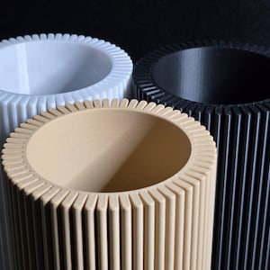 May include: Three cylindrical objects with ridged exteriors and circular openings. One is white, one is tan, and the other is black. The objects are arranged closely together, with the tan cylinder in the foreground.