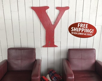 May include: A large red wooden letter Y is mounted on a white wood wall. Two burgundy leather armchairs are positioned on either side of the letter. A wicker basket filled with plaid blankets sits in front of the left armchair.