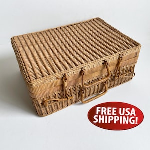 May include: A rectangular wicker picnic basket featuring a woven light brown natural fiber construction, a hinged lid, and two integrated woven handles on the front side. The basket has a structured design with a flat top and vertical weave pattern.