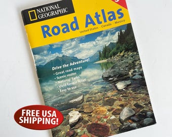 May include: A National Geographic Road Atlas from 1999. The cover features a scenic landscape with mountains and a lake. The title is in large blue and yellow letters. Includes the text "Drive the Adventure!" and "United States Canada Mexico".