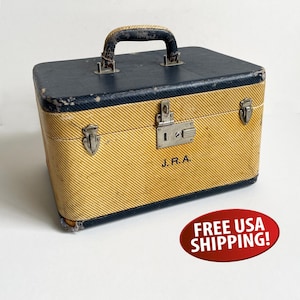 May include: A rectangular hard-sided travel case featuring a yellow and black diagonal striped pattern. The case has a dark blue top and base, a central metal locking latch, two side latches, and a top handle. The initials J. R. A. are printed in black.