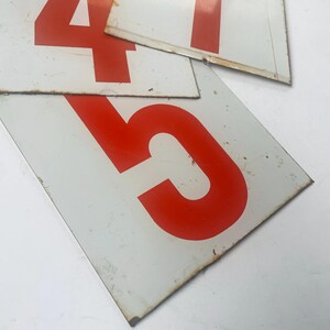May include: Close-up of three white metal signs with large, bold, red numbers. The numbers are 4, 5, and 1. The signs have a distressed appearance with some rust and wear around the edges, suggesting they are vintage or antique.